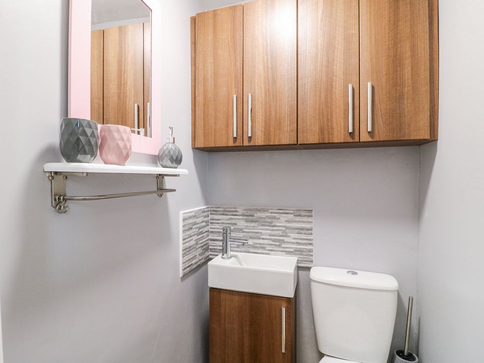 A bathroom with a toilet a sink wooden cabinets a mirror and decorative containers at Corner Cottage in Ashbourne