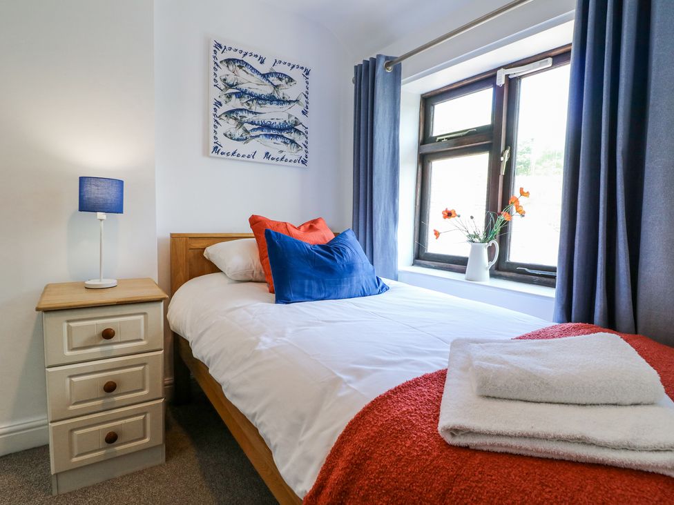 A bedroom with a single bed bedside table with a lamp window with curtains and flowers at Corner Cottage in Ashbourne