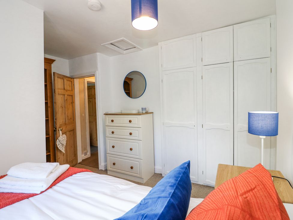 A bedroom with a bed with blue and orange pillows a white chest of drawers a blue lamp and built-in white wardrobes at Corner Cottage in Ashbourne