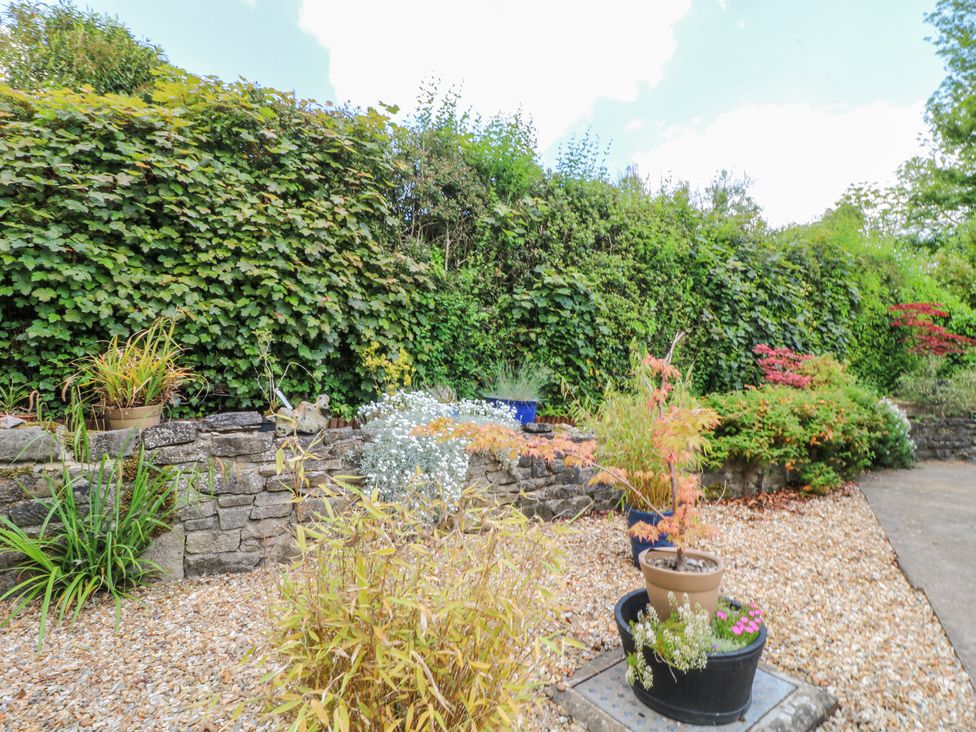 A garden area with potted plants gravel ground and a stone wall with green bushes at Corner Cottage in Ashbourne