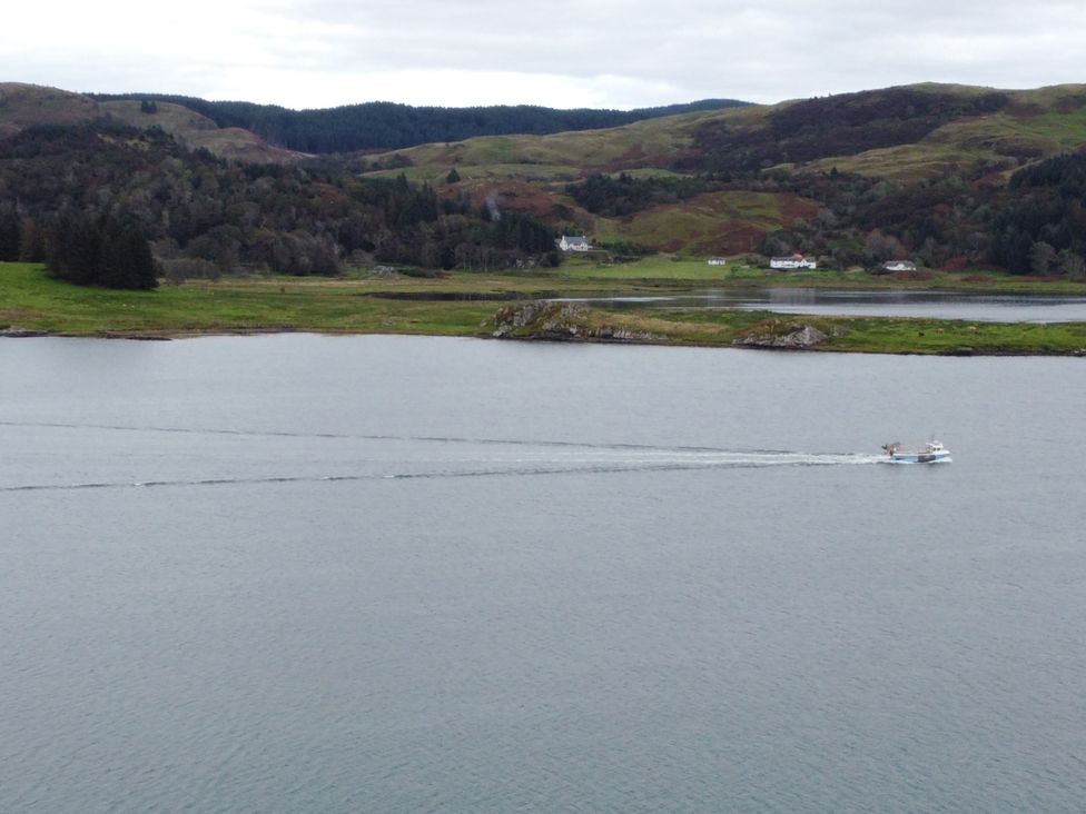 A boat on water with hills and houses in the background at Scarba in Balvicar, Isle Of Seil