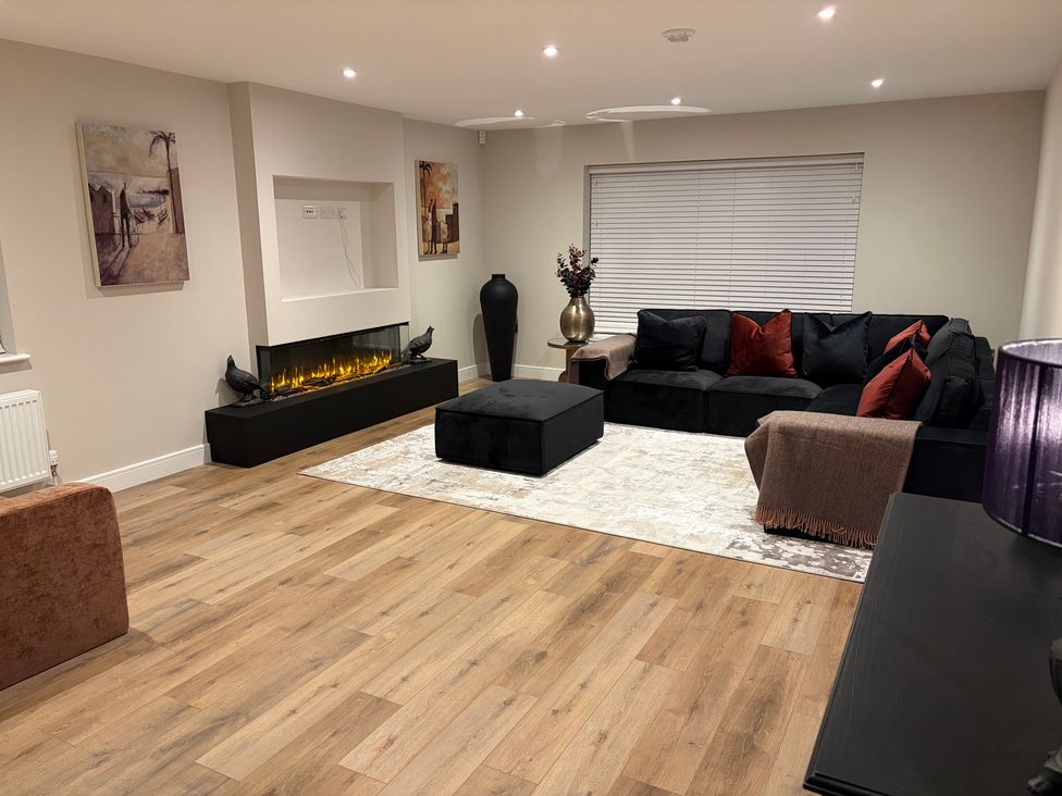 A living room with a sofa, ottoman, and fireplace at Cross Winds in Clapham