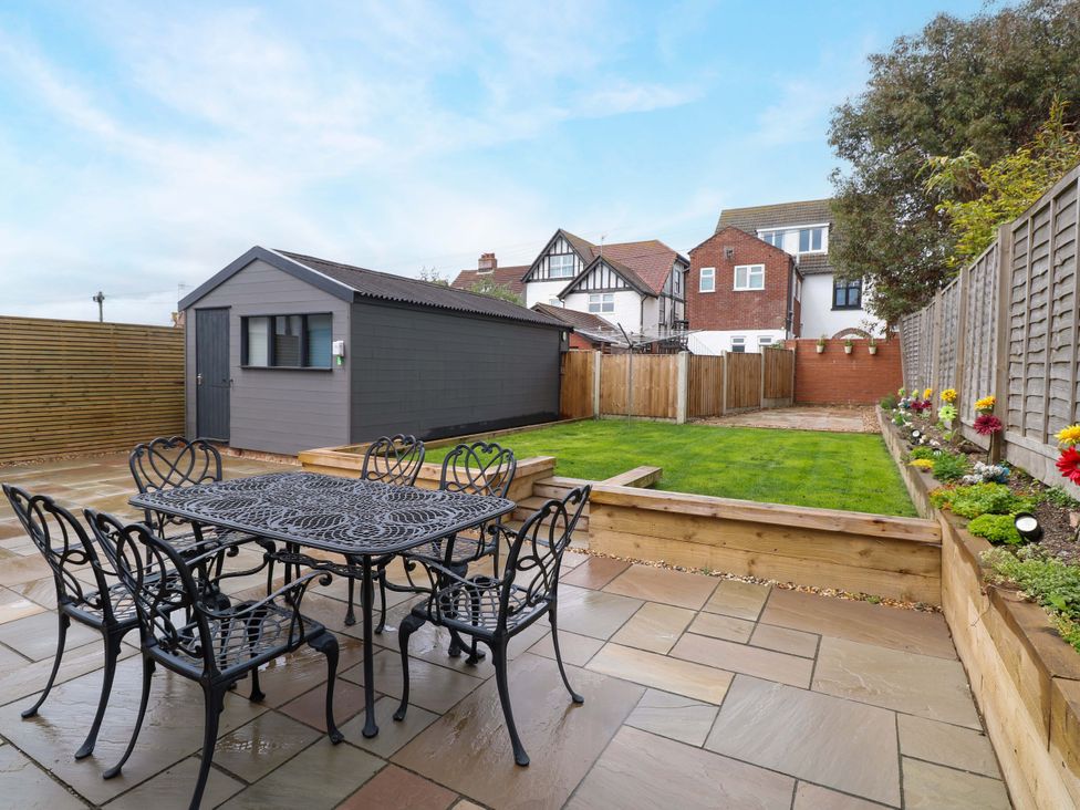 A garden with a dining table and chairs in front of a shed at Highland House in Sheringham