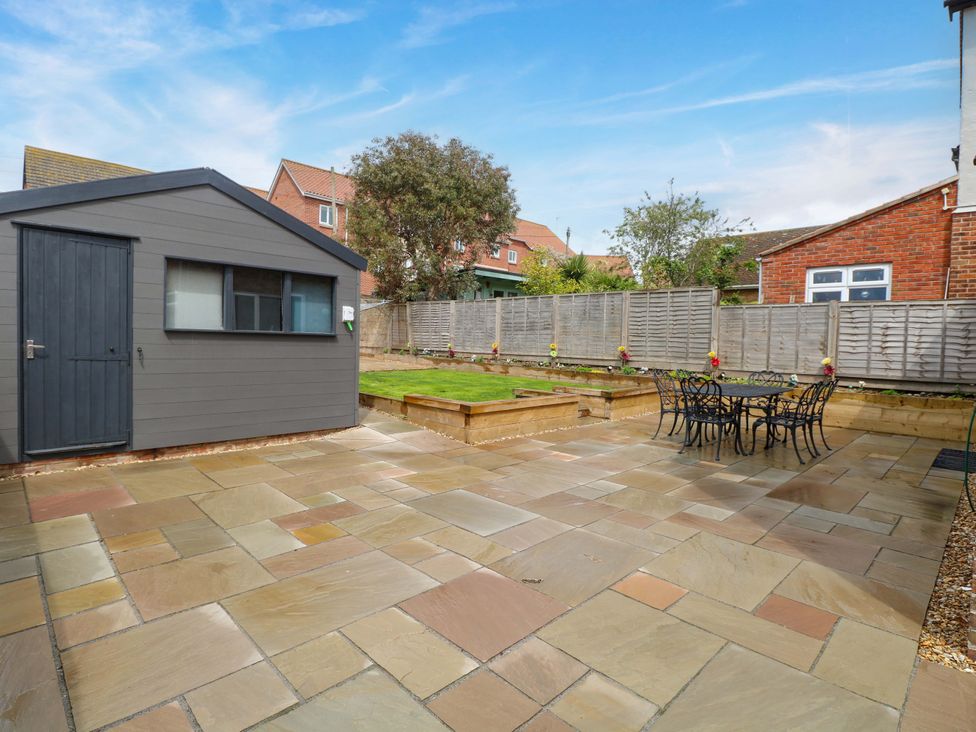 A garden with a patio, table and chairs near a shed at Highland House in Sheringham