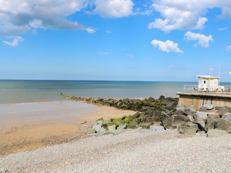 A beach with sand, rocks, sea, and a building at Highland House in Sheringham