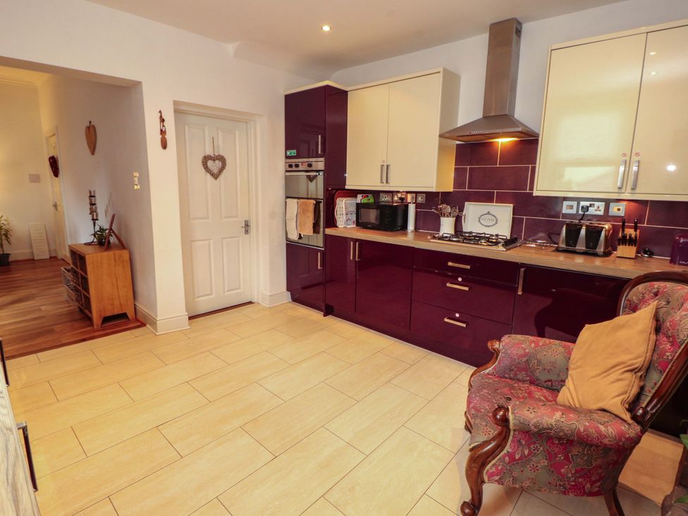 A kitchen with cabinets, an oven, microwave, kettle, and chair at 2 The Crescent