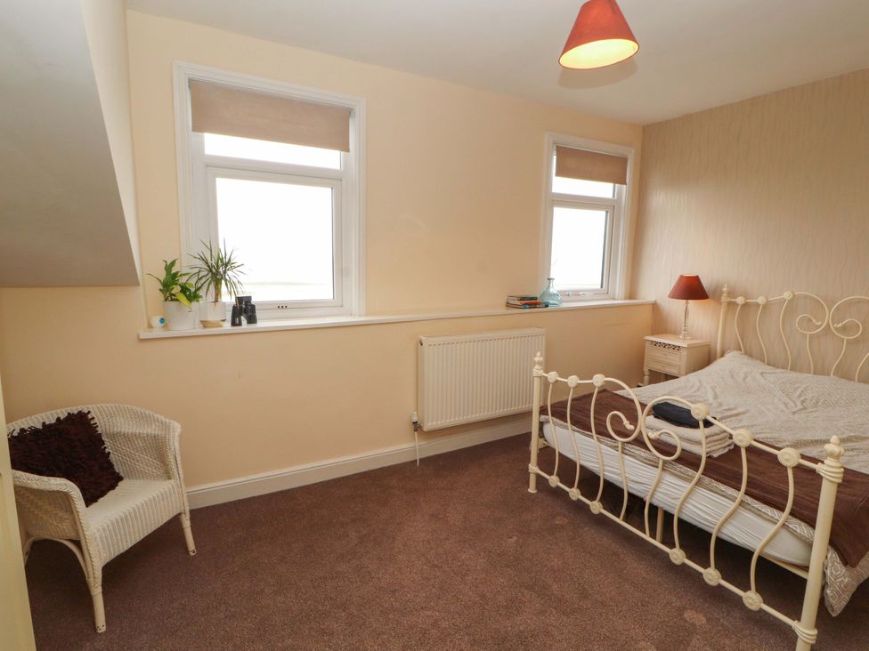 A bedroom with a bed, armchair and windows at 2 The Crescent