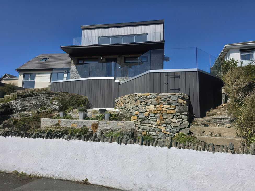 An outdoor view of a house with a glass railing and stone walls at Seaddler Trearddur Bay