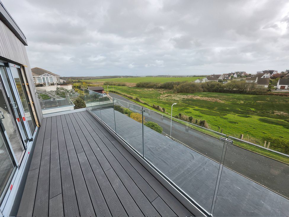 A balcony with glass railing overlooking a landscape at Seaddler in Trearddur Bay