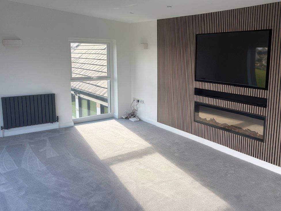 A living room with a window, radiator, television, and fireplace at Seaddler in Trearddur Bay