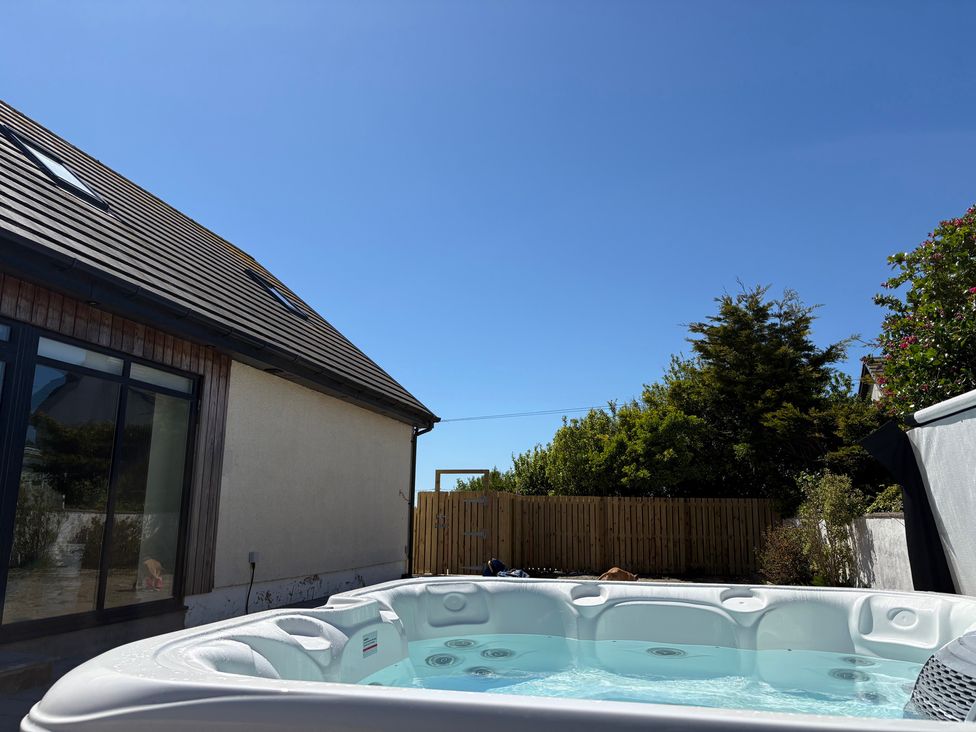 A hot tub near a house with a fence and trees at Seaddler in Trearddur Bay