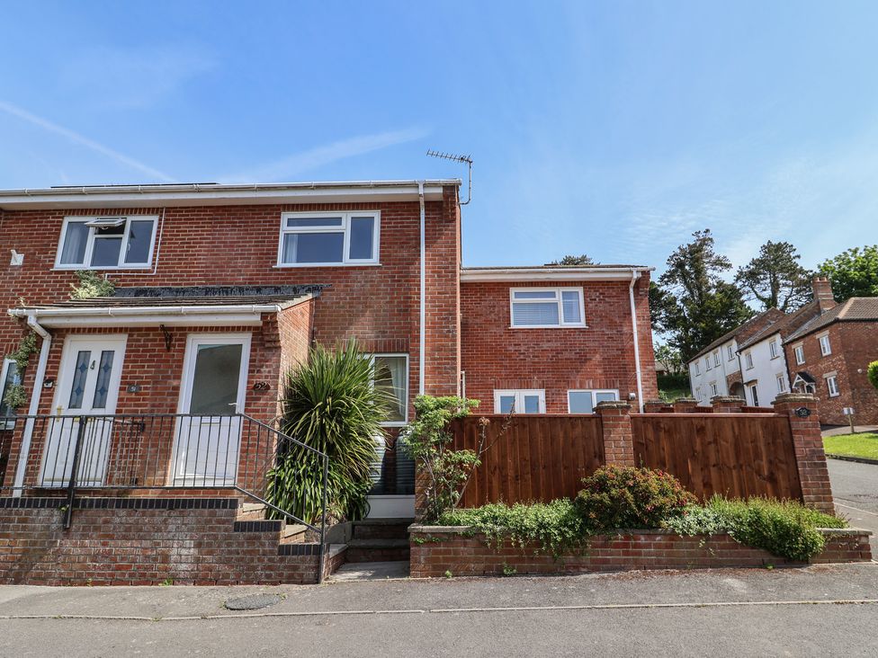 A brick residential building with two white doors and windows with plants and a wooden fence in front at SubLyme in Lyme Regis
