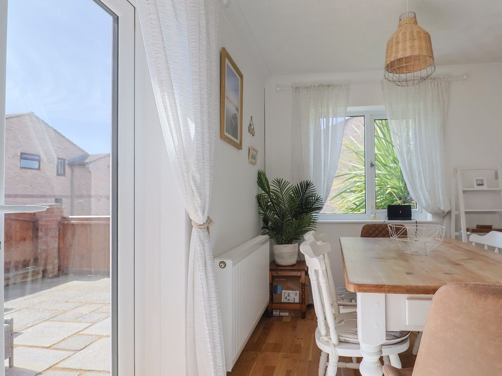 A dining room with a wooden table white chairs a plant near the window and a door leading outside at SubLyme in Lyme Regis