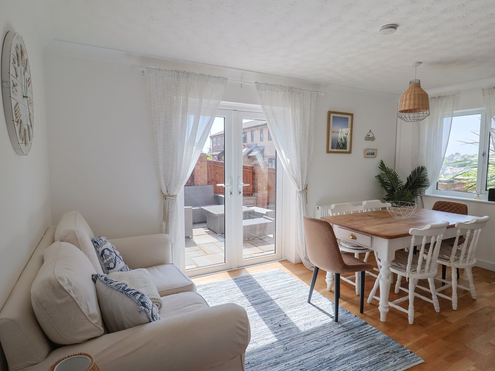 A dining area with a wooden table and chairs next to a small sofa and glass doors leading outside at SubLyme in Lyme Regis