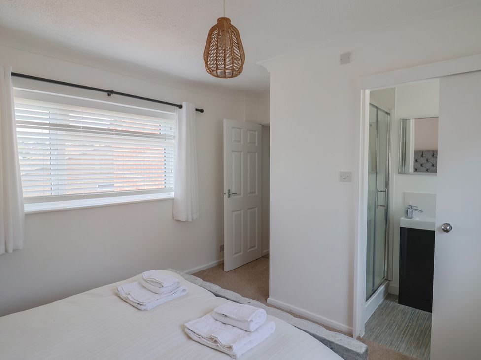 A bedroom with a bed holding folded towels a window with blinds a door and a bathroom with a shower at SubLyme in Lyme Regis