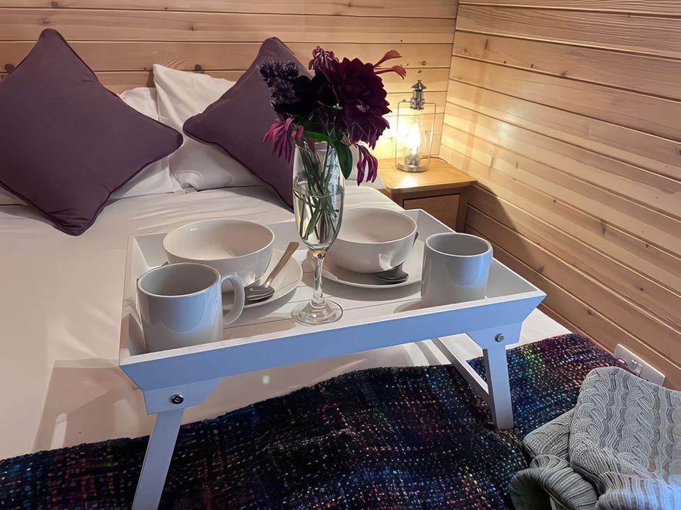 A bed with a tray containing mugs and bowls at Lakeside Pods - pets welcome Greenfield
