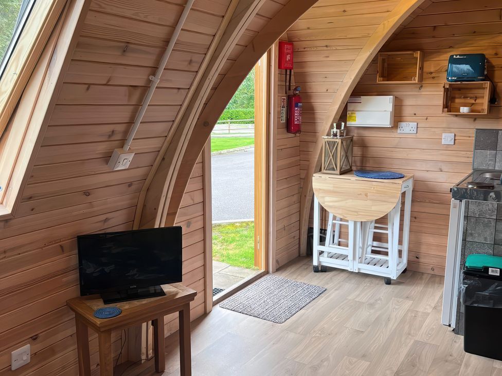 A kitchen area with a television and wooden table at Lakeside Pods - pets welcome Greenfield