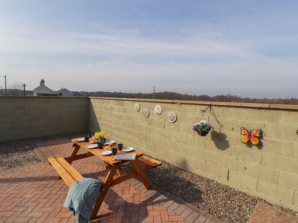 An outdoor dining area with a wooden table and plates at Daisy Cottage near Wigton