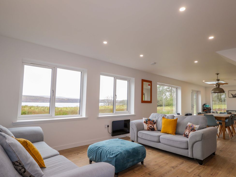 A living room with a sofa, ottoman, and dining area at Faodail House in Portree