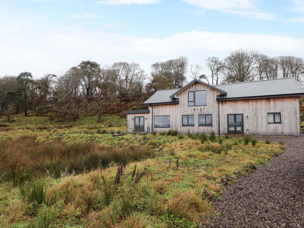 An exterior view of a wooden house surrounded by grass and trees at Faodail House Portree