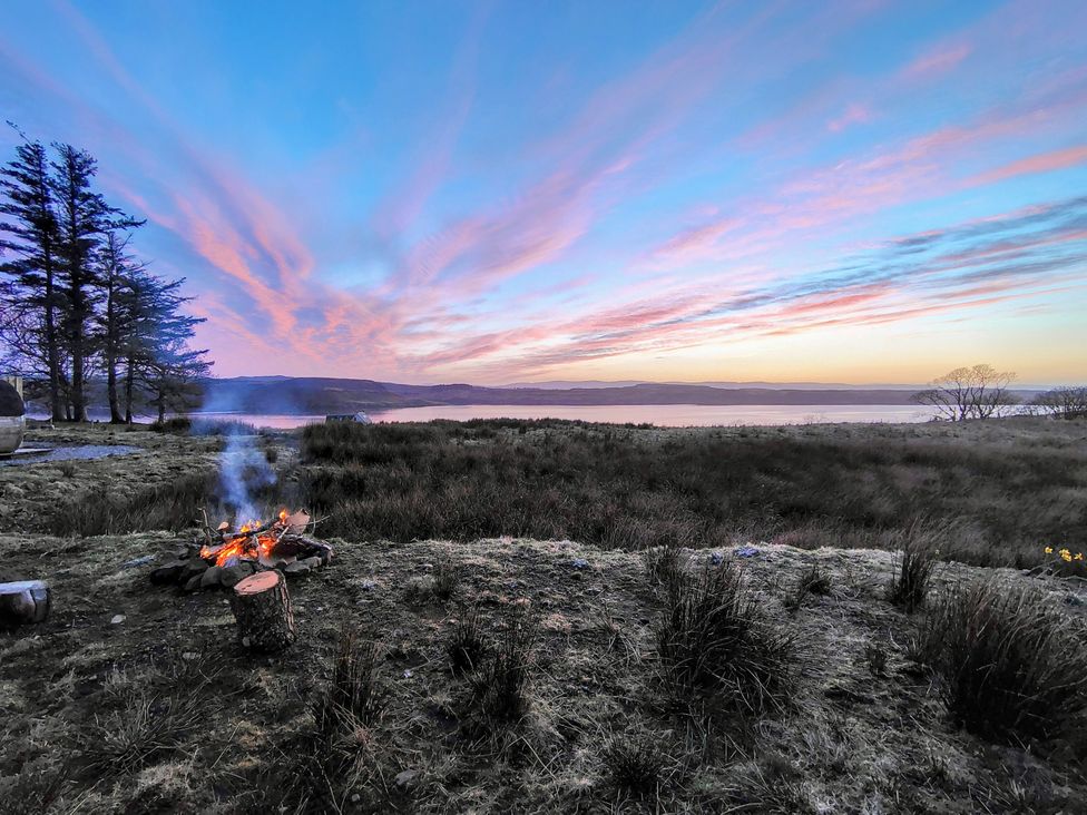 An outdoor scene with a fire pit and lake view at Faodail House Kingsburgh near Uig