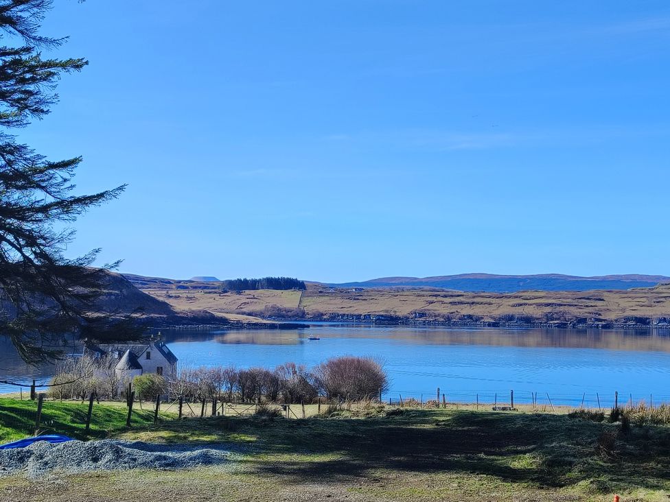 A view of a house by the water with hills and trees at Faodail House Kingsburgh near Uig