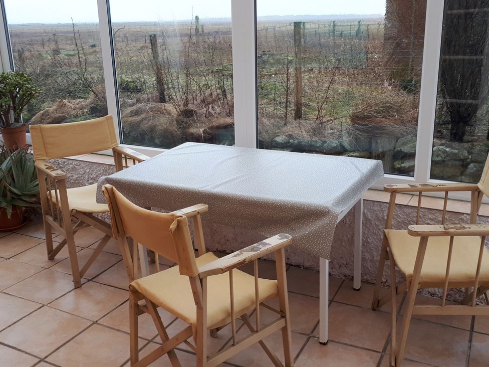 A table with four chairs and a plant in a conservatory at Taigh Phinc, Balemore near Lochmaddy, North Uist