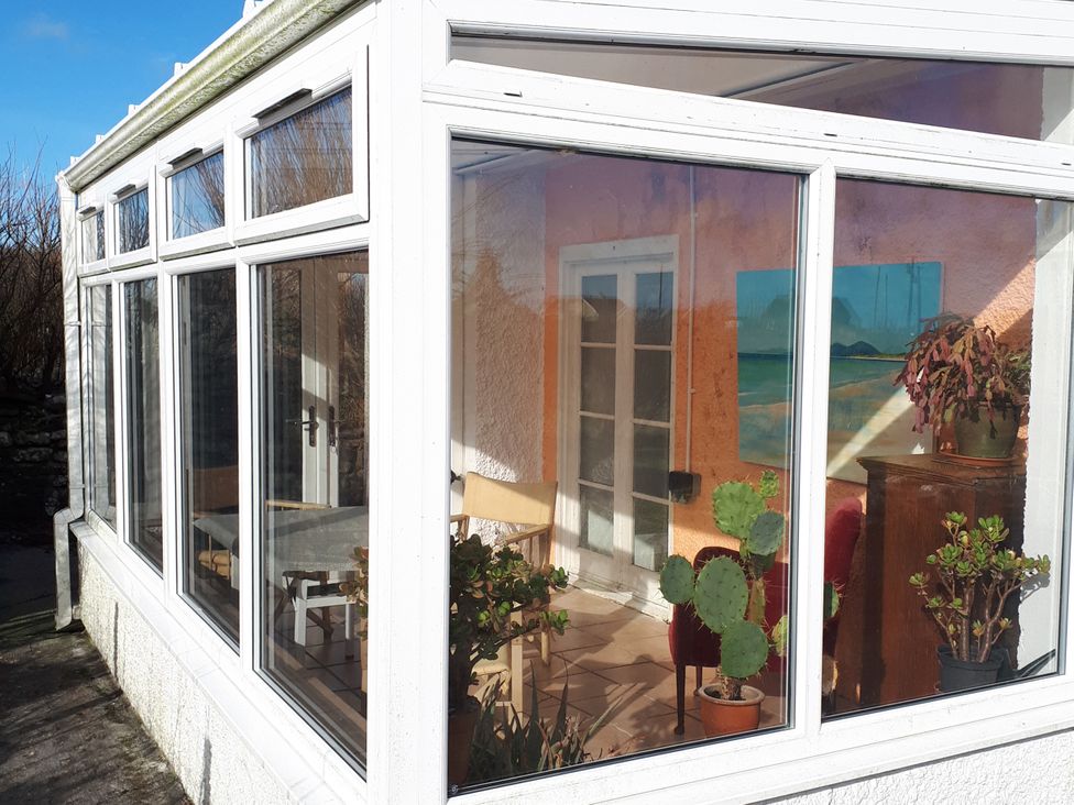 A conservatory with plants and a table at Taigh Phinc Balemore near Lochmaddy, North Uist