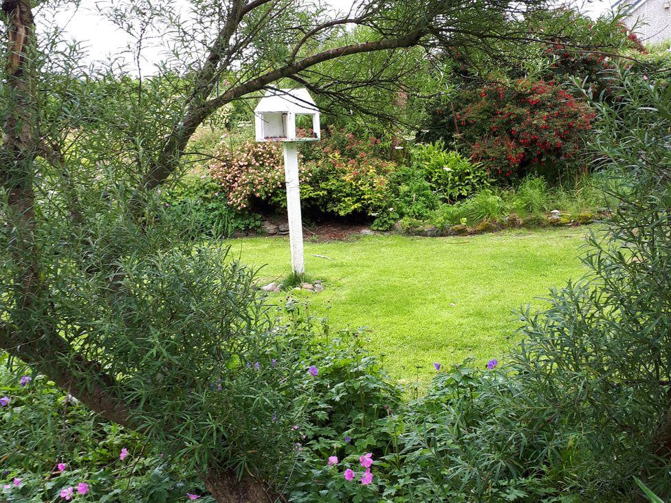 A garden with a bird feeder and flowering plants at Taigh Phinc, Balemore near Lochmaddy, North Uist