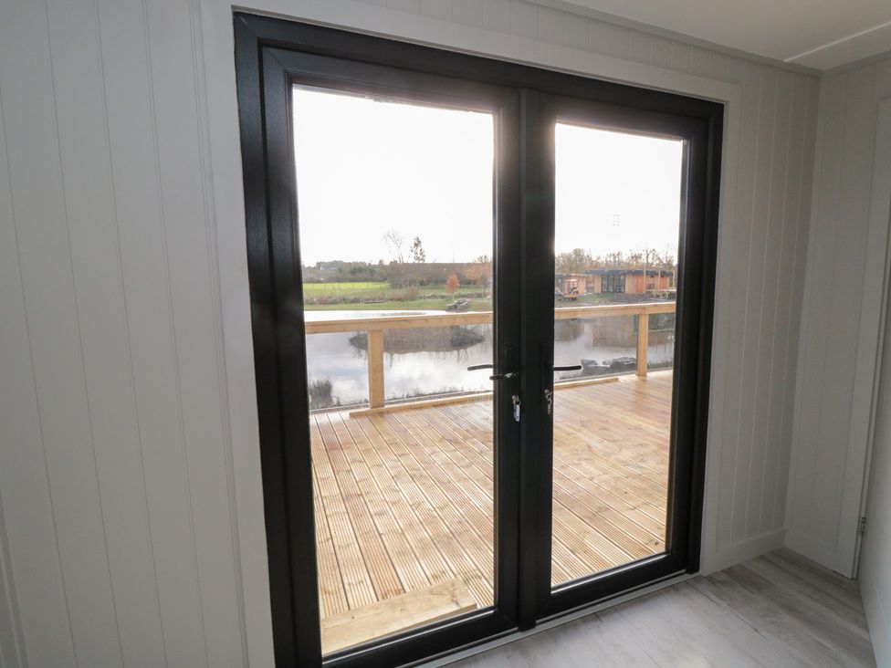 A living room with double doors leading to a wooden deck and water view at Lodge 6 Stockton-on-Tees