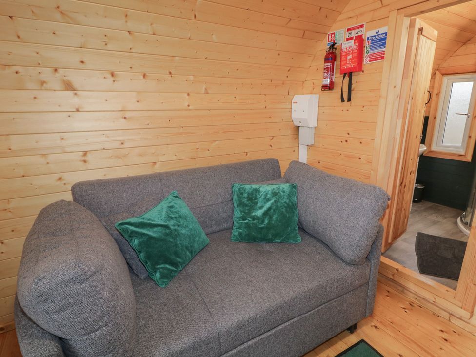 A gray sofa with two green pillows in a wooden room next to a small bathroom at Hawthorn in Dungiven Londonderry