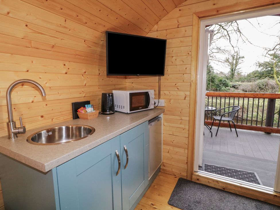 A kitchen area with a sink microwave coffee maker small fridge and a door leading to a balcony with chairs at Hawthorn in Dungiven Londonderry
