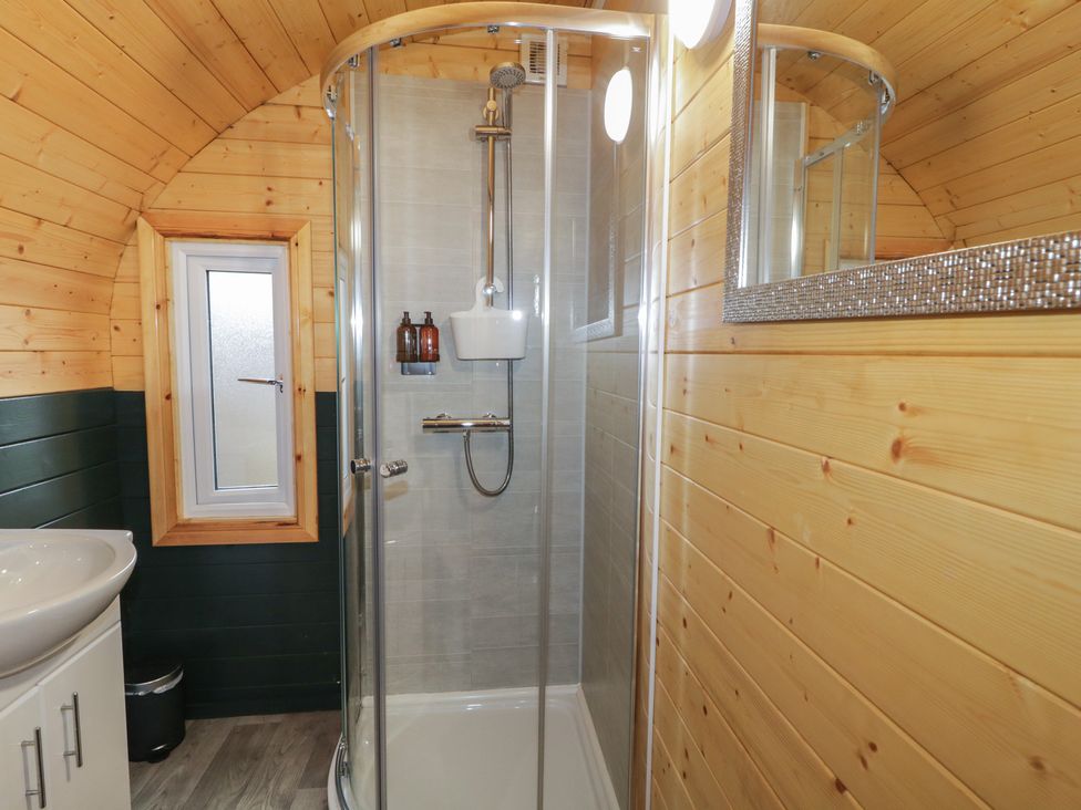 A bathroom with a corner glass shower enclosure a sink with a cabinet a small window and wooden paneled walls at Hawthorn in Dungiven Londonderry