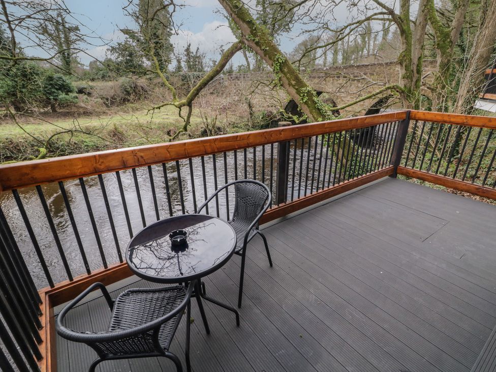 A balcony with a round glass table and two black chairs overlooking a river with trees at Hawthorn in Dungiven Londonderry
