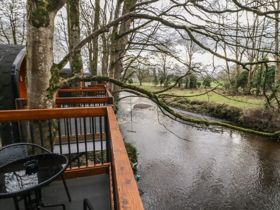 A balcony with a round table and chairs overlooking a river with trees at Hawthorn in Dungiven Londonderry