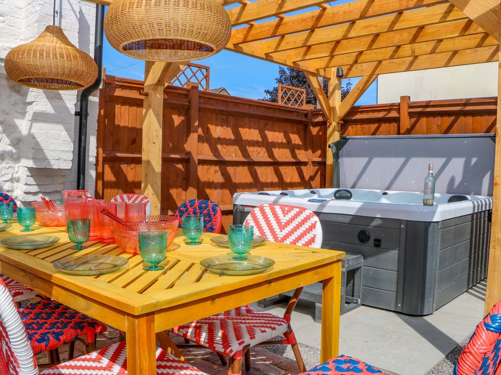 An outdoor patio with a wooden table and chairs alongside a hot tub at Spring Cottage in Arundel, West Sussex