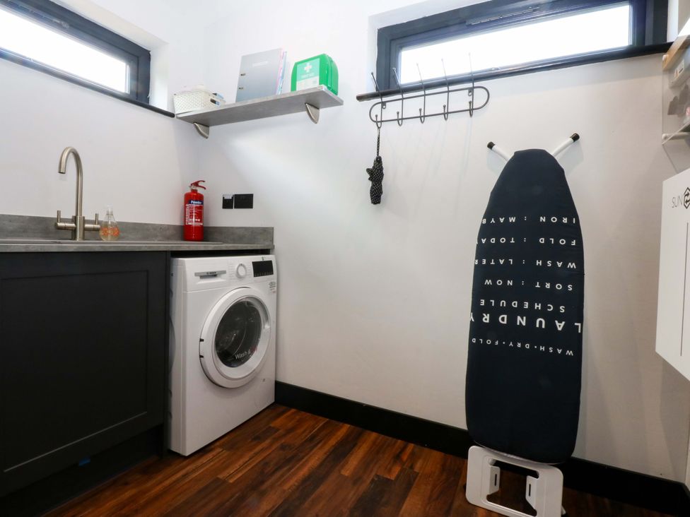 A laundry room with a washing machine and an ironing board at Y Cwt in Moelfre