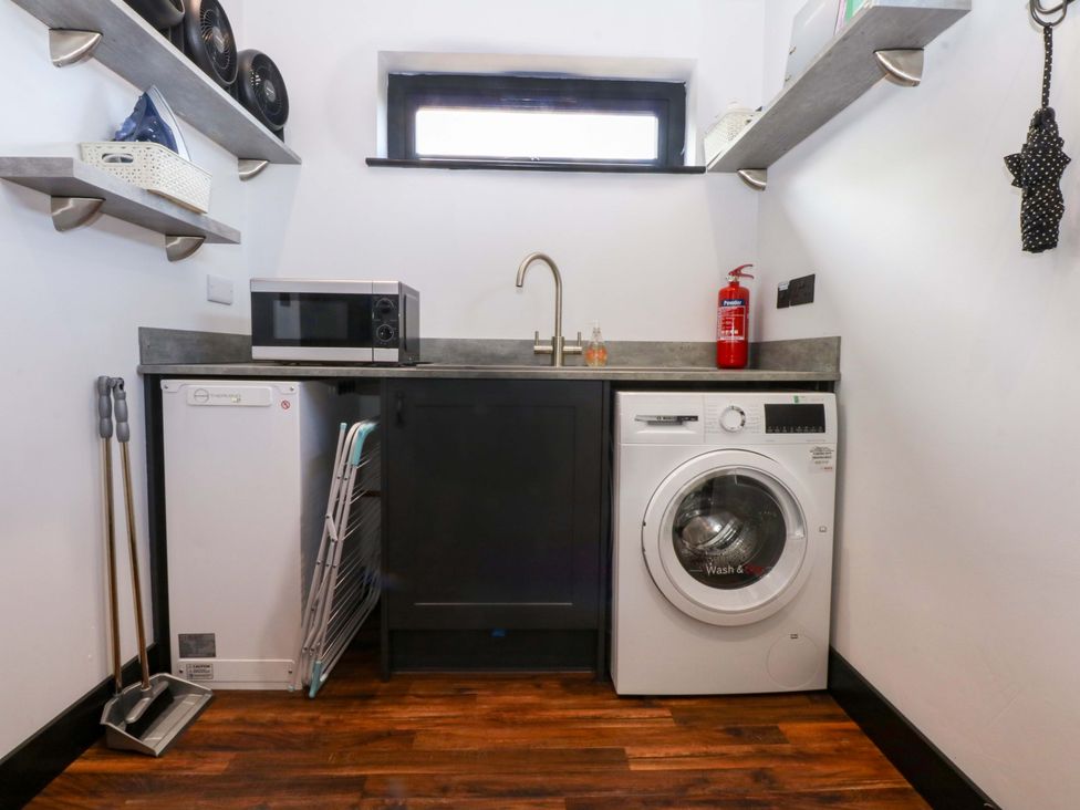 A laundry room with a washing machine and microwave at Y Cwt, Moelfre