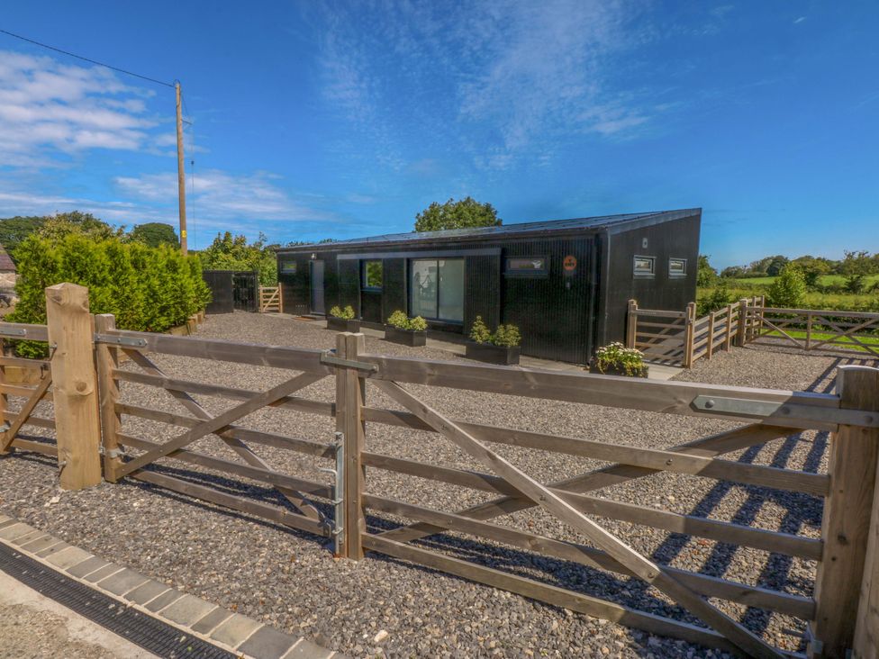 An outdoor view of a black house with a gate and gravel area at Y Cwt in Moelfre