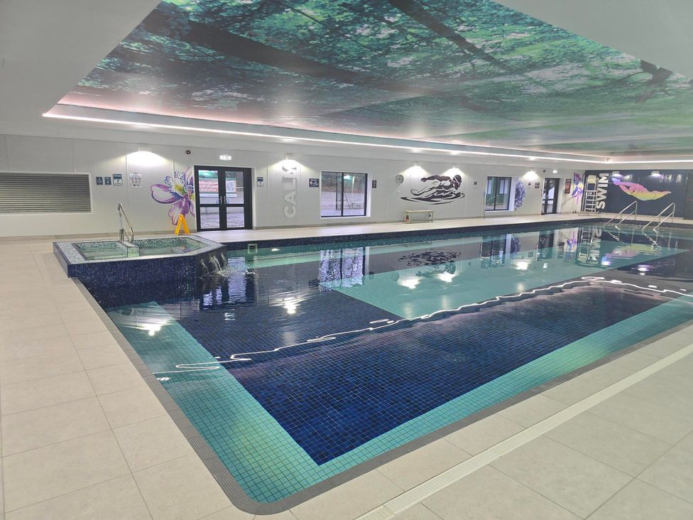 An indoor swimming pool with steps and windows at Cornish Woodland Retreat near St Tudy