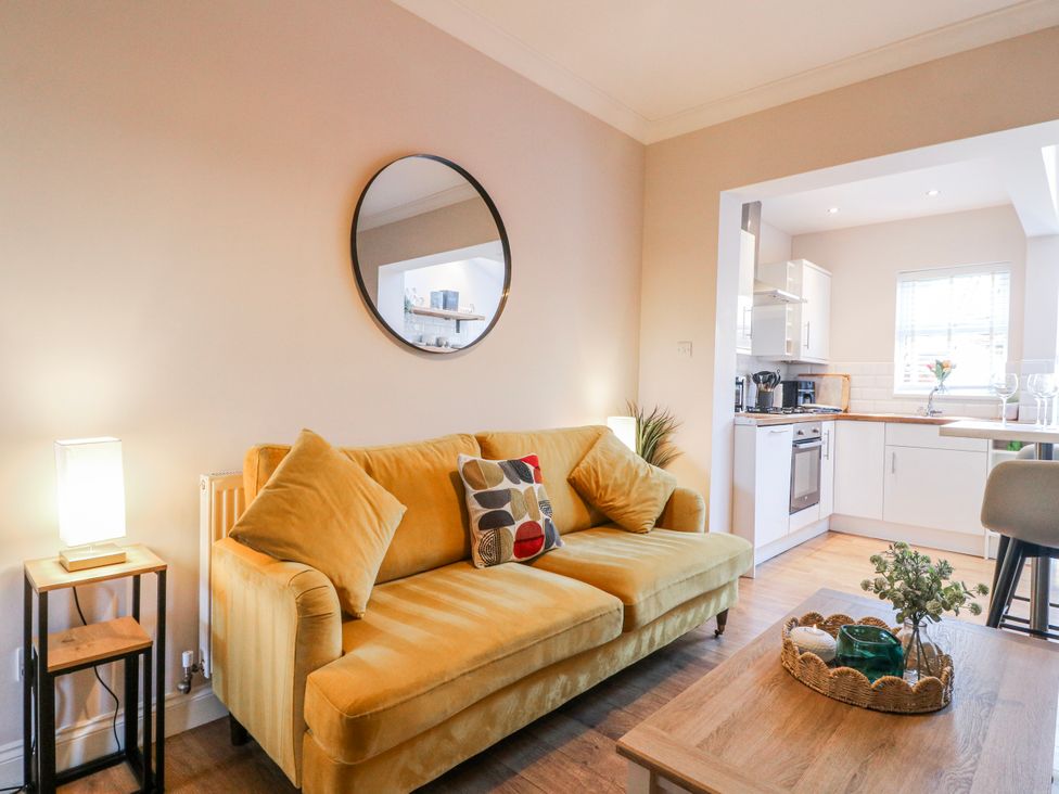A living room with a yellow sofa and kitchen view at Hill View Cottage Ashbourne
