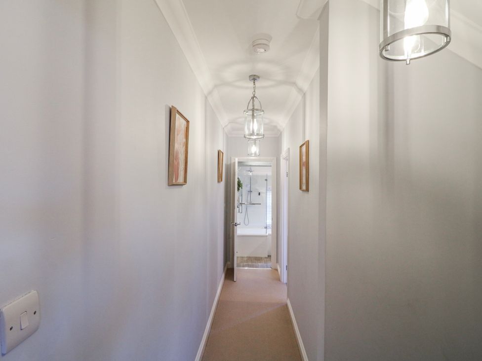 A hallway with light fixtures and wall art leading to a bathroom at Hill View Cottage in Ashbourne