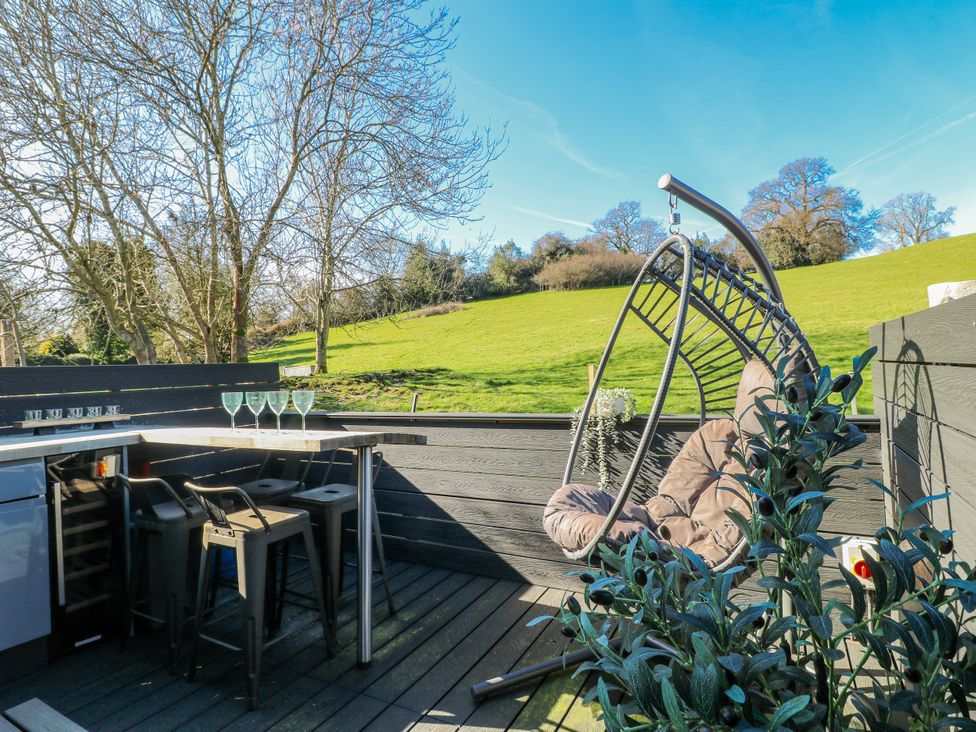 An outdoor seating area with a hanging chair and bar stools at Hill View Cottage Ashbourne