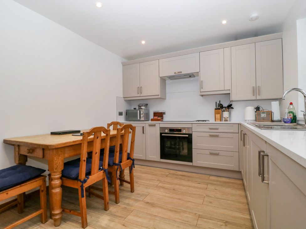 A kitchen with cabinets, oven, sink, and dining table at Capella Cottage in Keswick