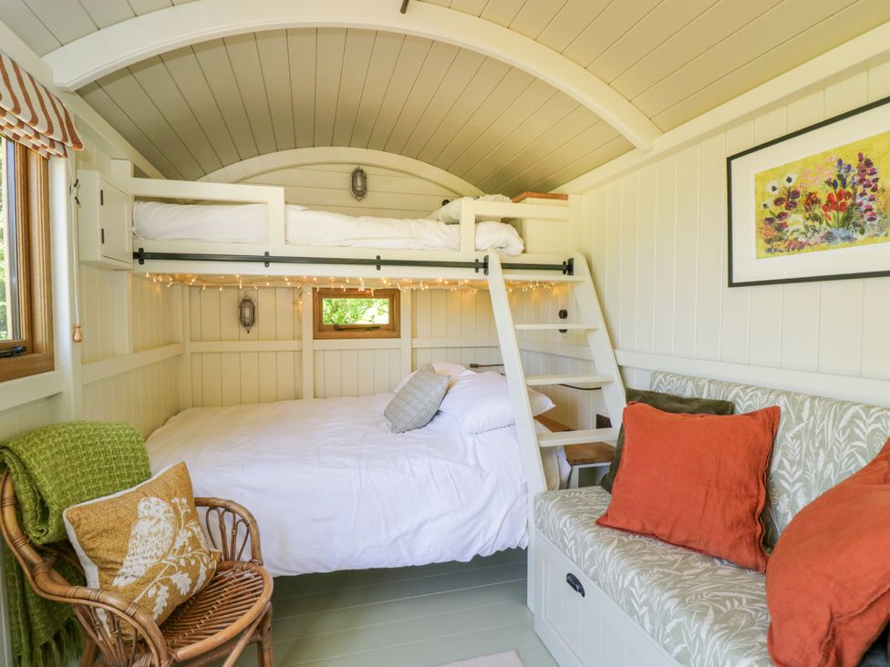 A bedroom with bunk beds a wicker chair with a cushion a small sofa with orange pillows and a painting on the wall at Blackthorn in South Leigh near Witney