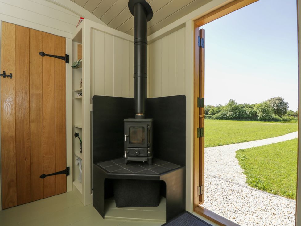 A wood stove in a corner with a wooden door and an open door showing a grassy outdoor area at Blackthorn in South Leigh near Witney