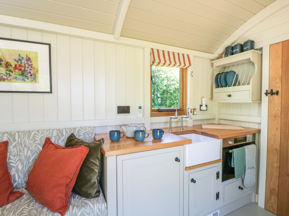 A kitchen with wooden countertops a white sink blue mugs and plates a small oven and a cushioned bench with pillows at Blackthorn South Leigh near Witney