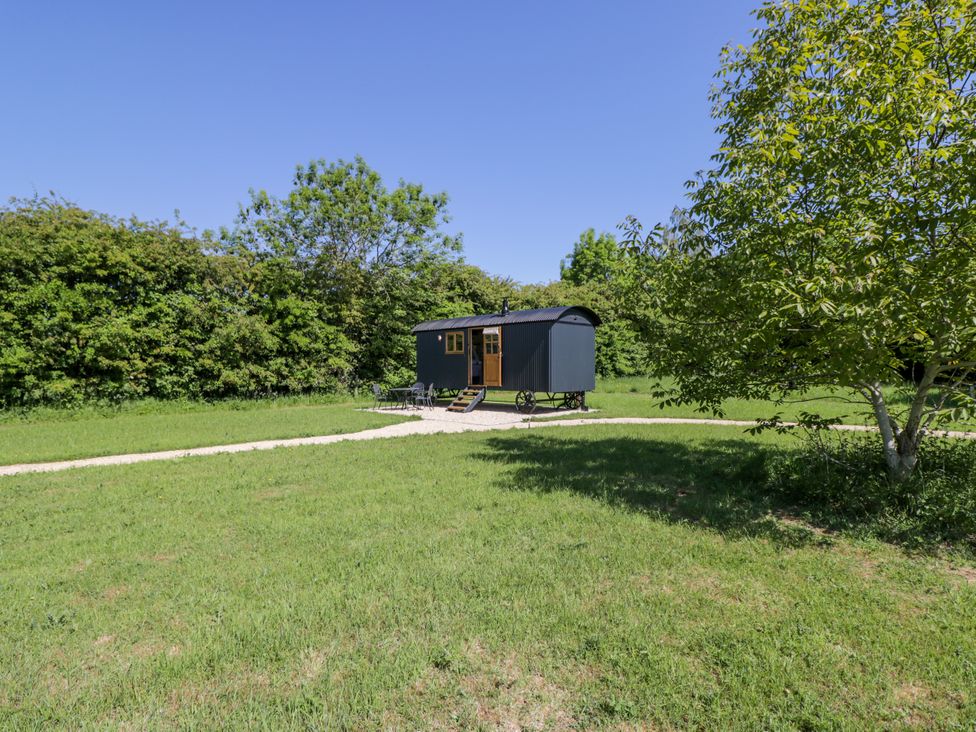 A small black shepherd hut on wheels with steps on a grass field surrounded by trees at Blackthorn South Leigh near Witney