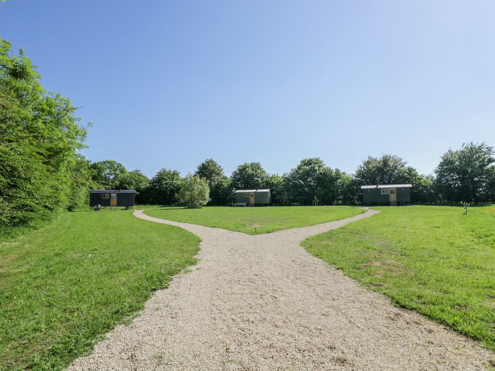 A gravel pathway splitting in a grassy field leading to three small cabins with trees in the background at Blackthorn in South Leigh near Witney