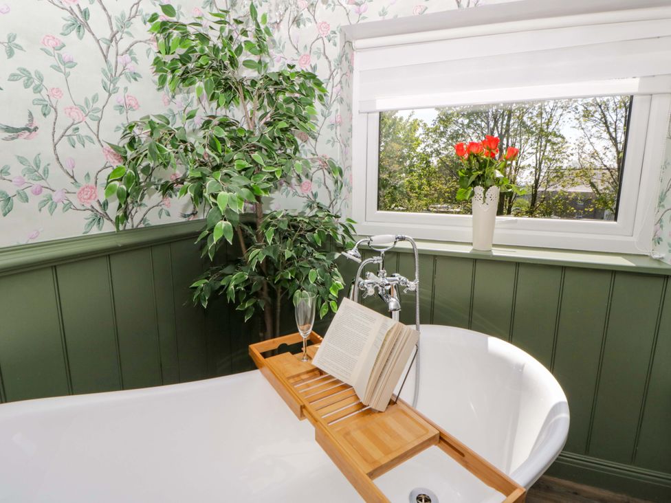 A bathroom with a bathtub and a shelf holding a book and glass at La Bastille in Maenclochog